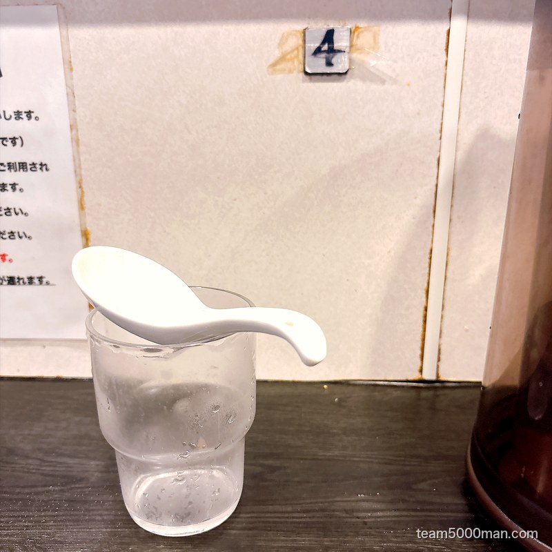豚星。カウンター席の卓上。セルフで用意した水とレンゲ、壁に席番号の4
