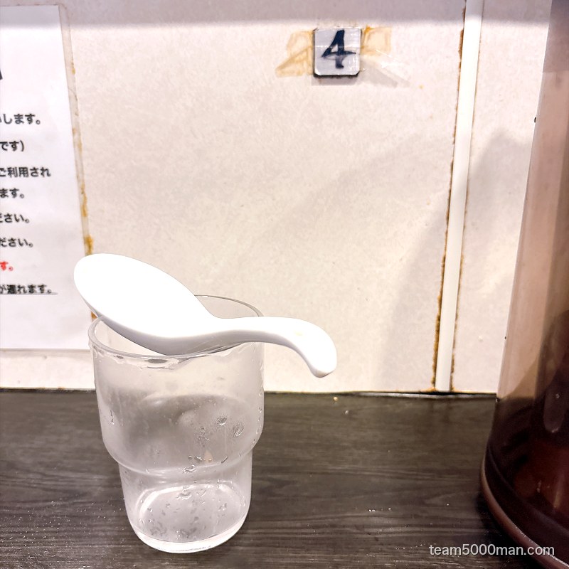 豚星。カウンター席の卓上。セルフで用意した水とレンゲ、壁に席番号の4