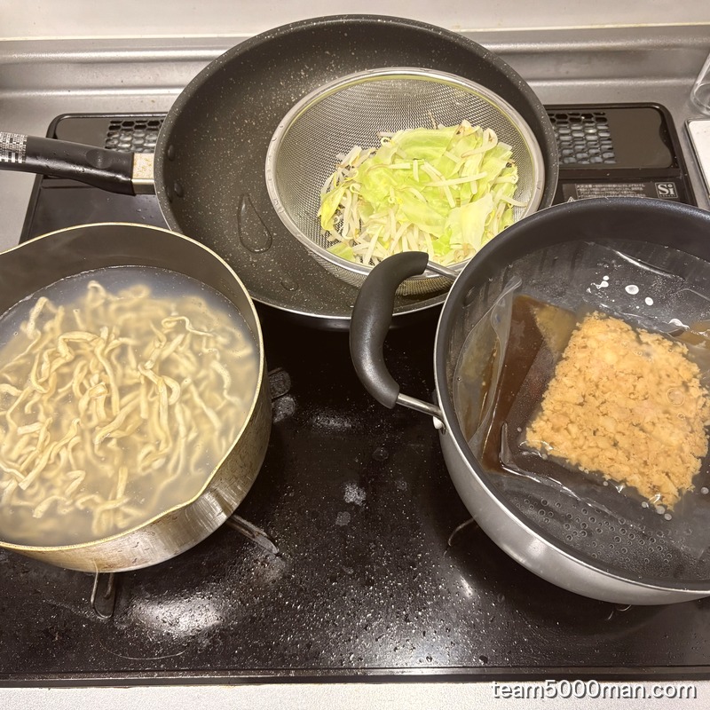 俺の生きる道 夢のラーメンの調理中。茹で上がった麺、湯せん中の味付け脂、ザルのキャベツともやし
