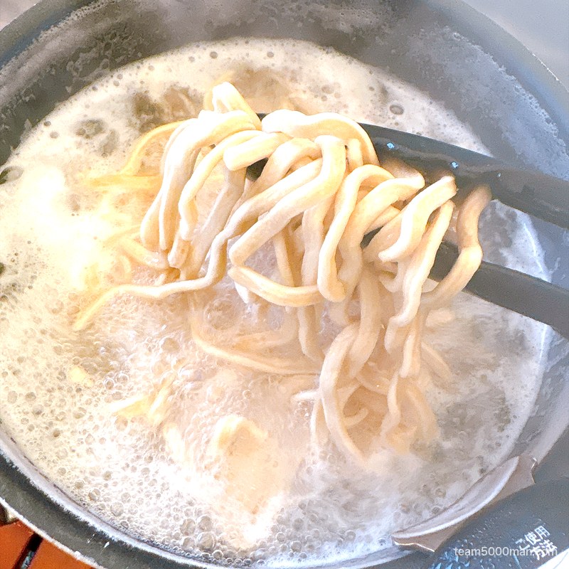 麺でる ラーメン カセットコンロで茹でている中太麺をトングで持ち上げたところ