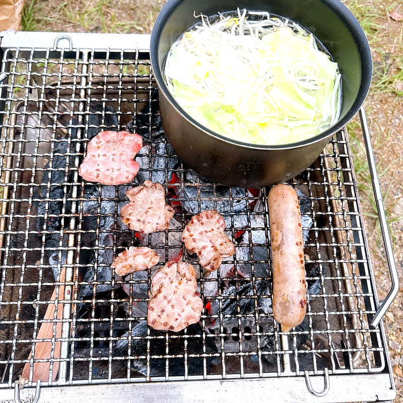 キャンプで宅麺 焚き火台の網の上で野菜を茹でる鍋と焼いている肉